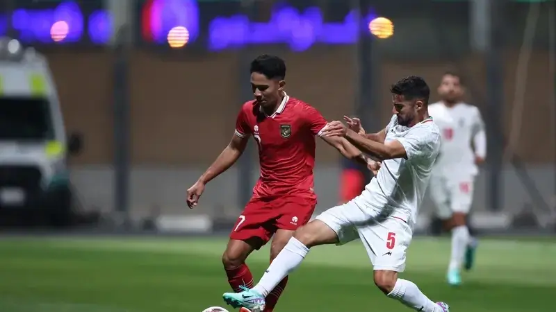 Iranian player in red controls the ball in a match at night.