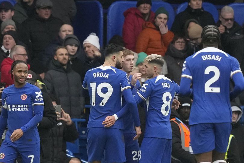 Chelsea players in blue kits celebrate together on the pitch with the crowd visible in the background during their match against Fulham.