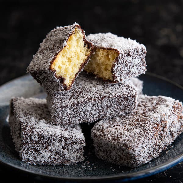 A baker carefully dipping sponge cake squares into chocolate icing, preparing to roll them in coconut for making Lamingtons.