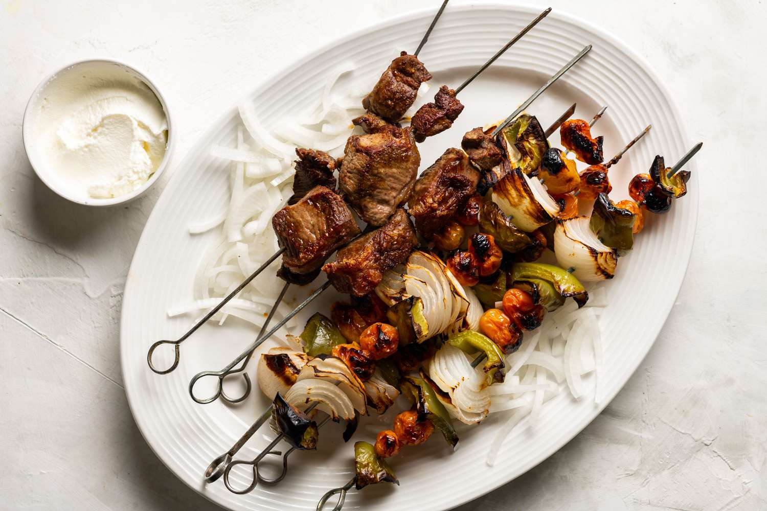 A plate of shashlik served with fresh vegetables and pita bread. 